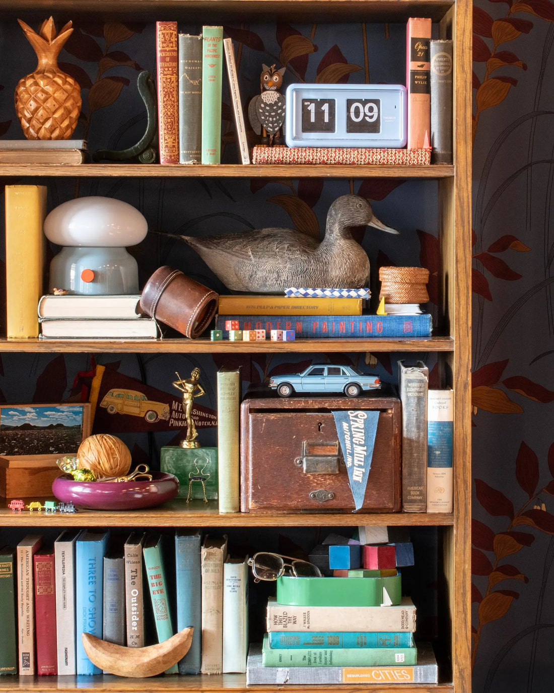 Whimsical bookshelf filled with vintage books, a duck figurine, clock, lamp, toy car, and curiosities