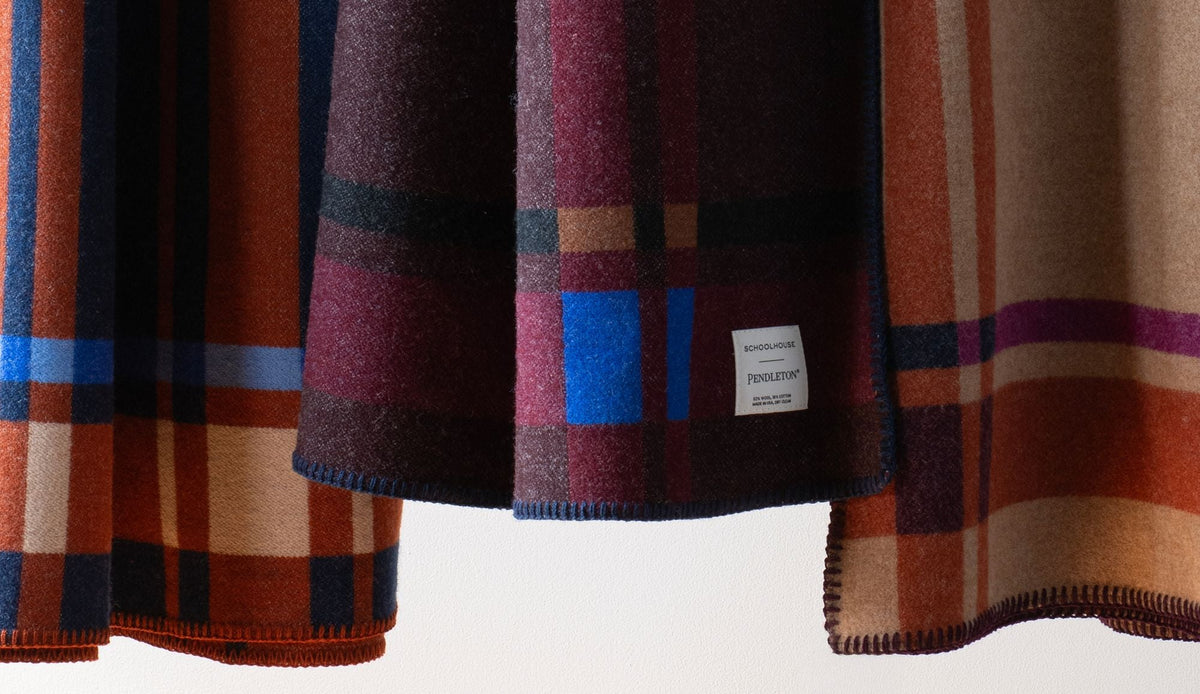 Close-up of plaid blankets showcasing multicolor woven patterns and stitched edges against a white background