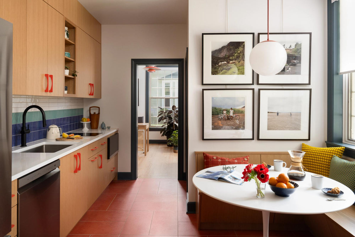 Modern kitchen and dining area with wood cabinetry, colorful tile backsplash, framed artwork, and round breakfast table