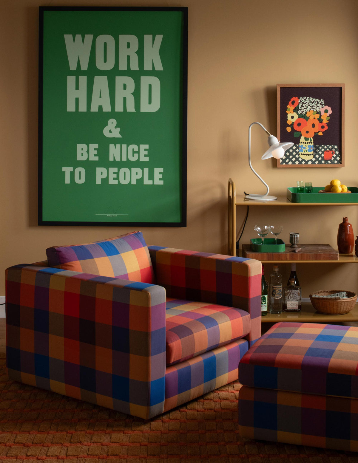 Miller cart styled with a lamp, trays, glasses, and lemons beside plaid chairs and a WORK HARD AND BE NICE TO PEOPLE poster
