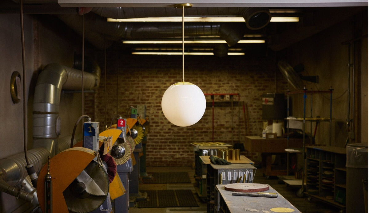 Natural brass rod pendant with opal glass globe shade hanging in a lighting workshop