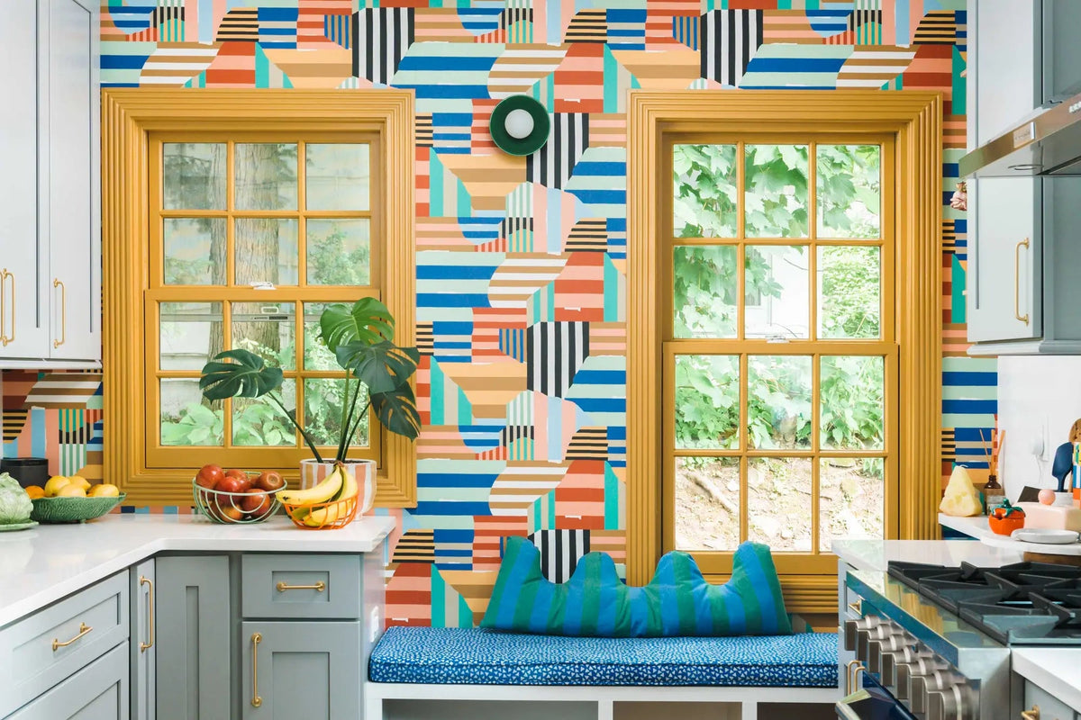 Remodeled kitchen with colorful geometric wallpaper, mustard-framed windows, pale blue cabinets, and a built-in window seat