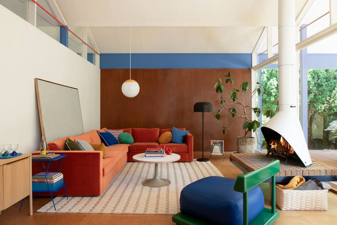 Midcentury-inspired living room with burnt-orange sectional sofa, blue ottoman, hanging globe pendant, white cone fireplace and garden-facing windows