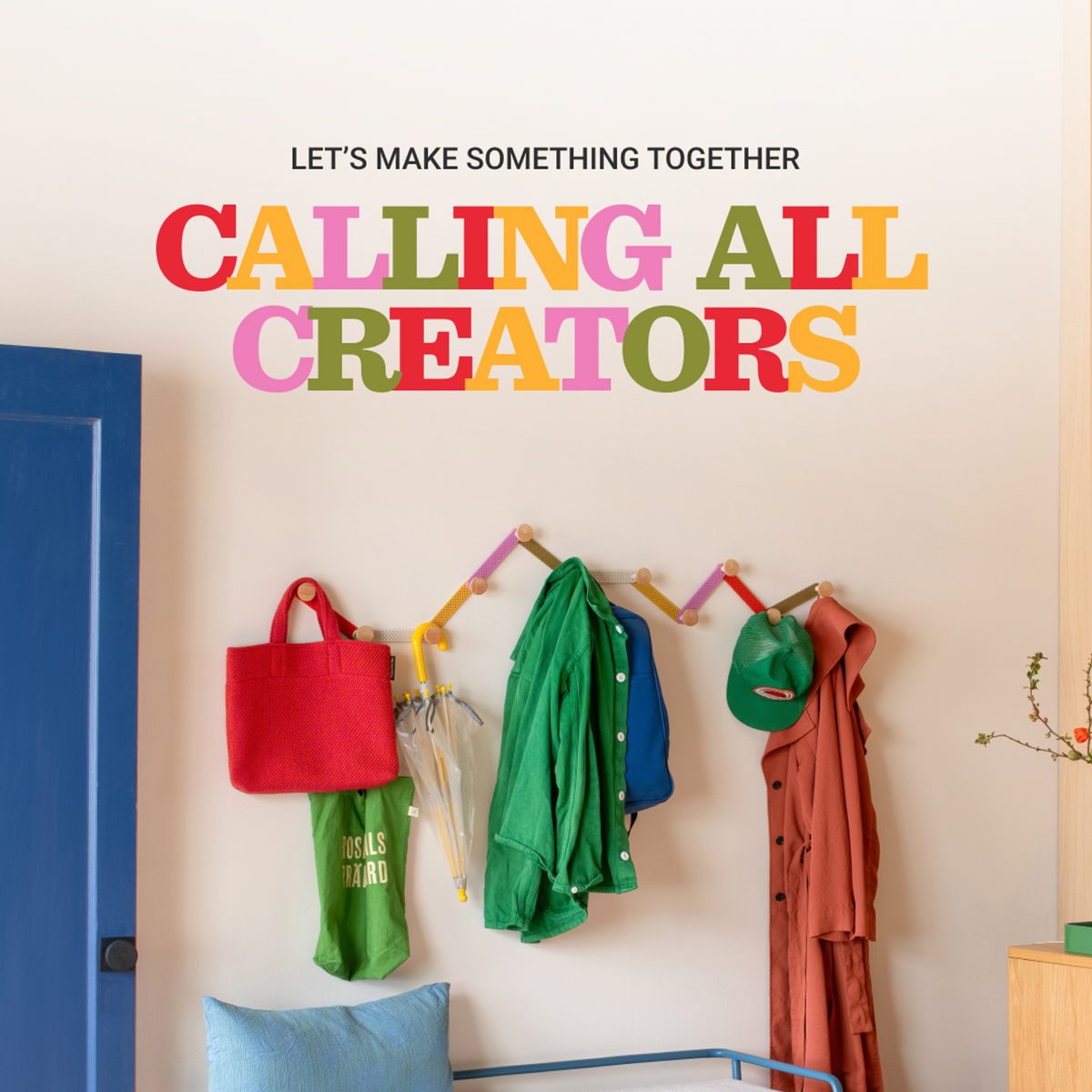 Colorful bags, coats, and umbrellas hang on a wall beneath Let’s Make Something Together Calling All Creators