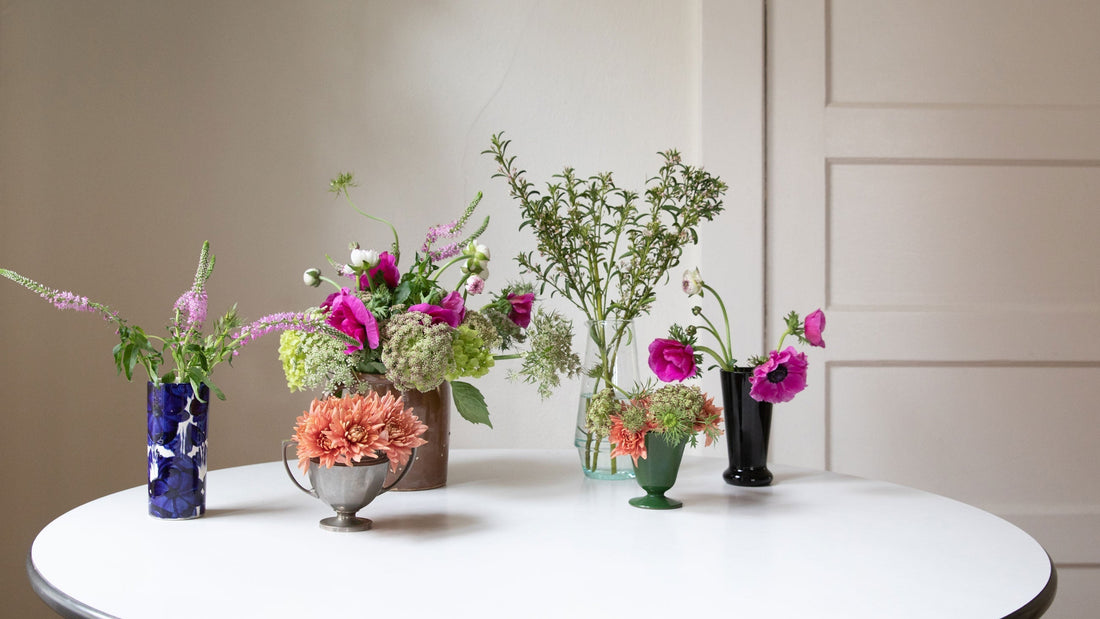 Several small mixed floral arrangements with bright pink and orange blooms on a round white table against a cream wall