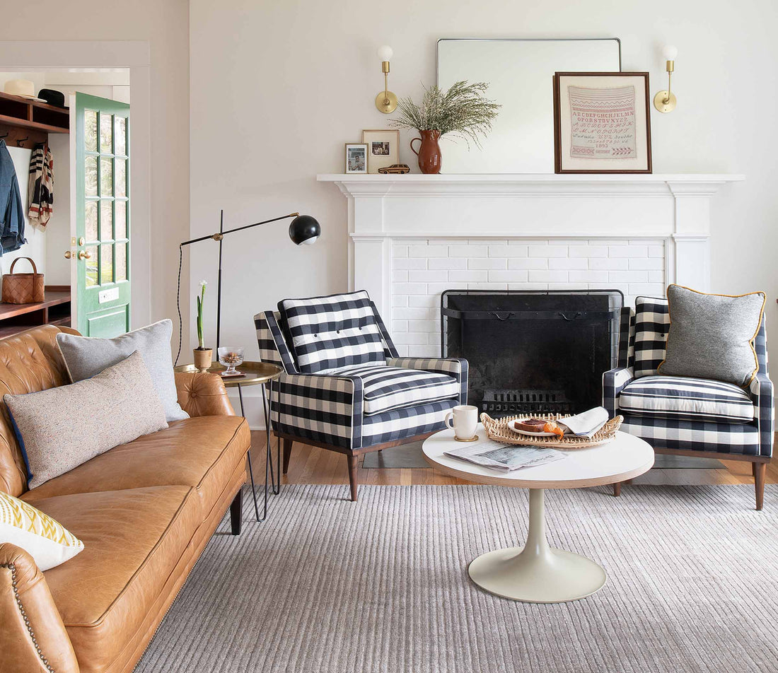 Living room with a tan leather sofa and black-and-white buffalo check armchairs arranged around a white fireplace