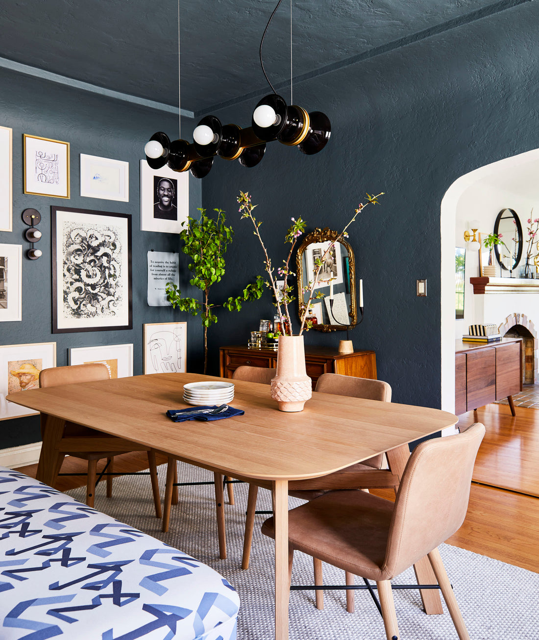 Regent chandelier suspended over a wood dining table in a moody dining room with dark teal textured walls and a gallery wall