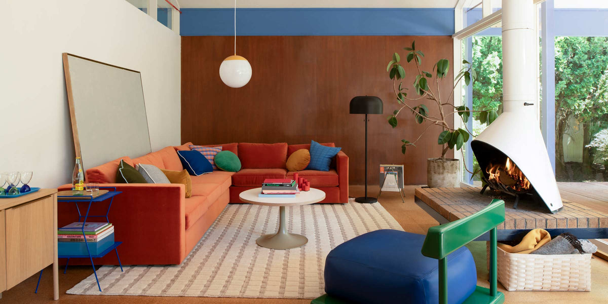Orange sectional sofa on a patterned wool rug in a living room with a white cone fireplace and large window