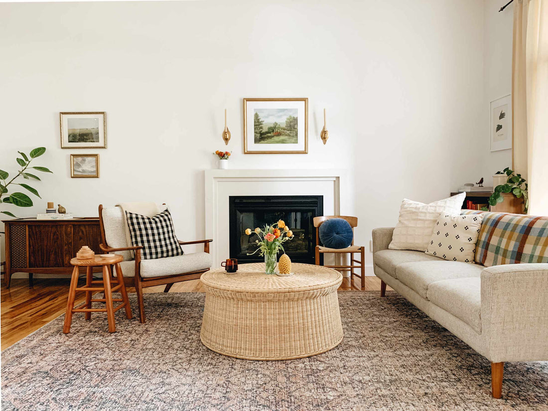 Cozy living room with a centered fireplace, round woven rattan coffee table, mid-century armchairs and a neutral sofa styled with patterned pillows