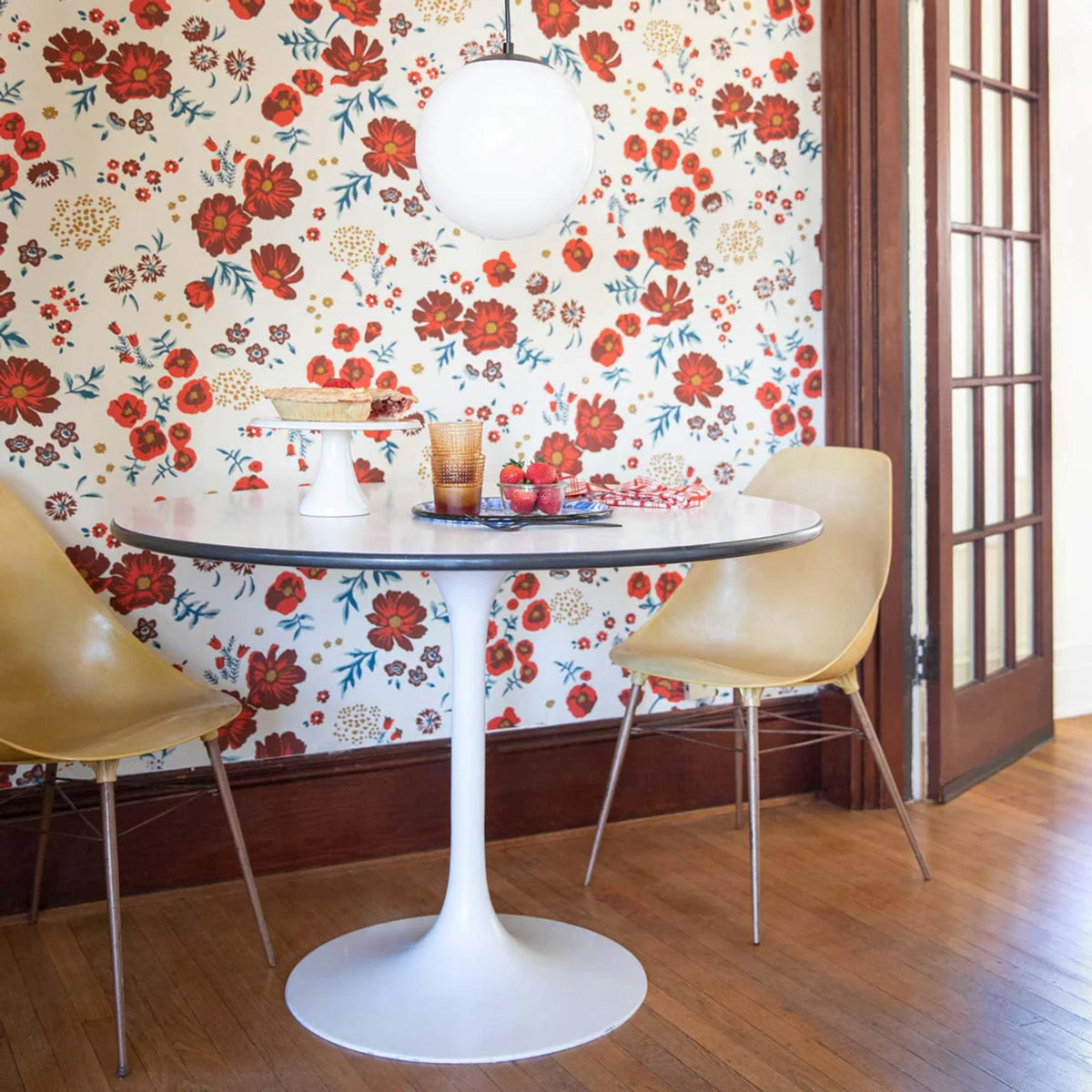 Dining area with a round table and chairs against colorful floral wallpaper