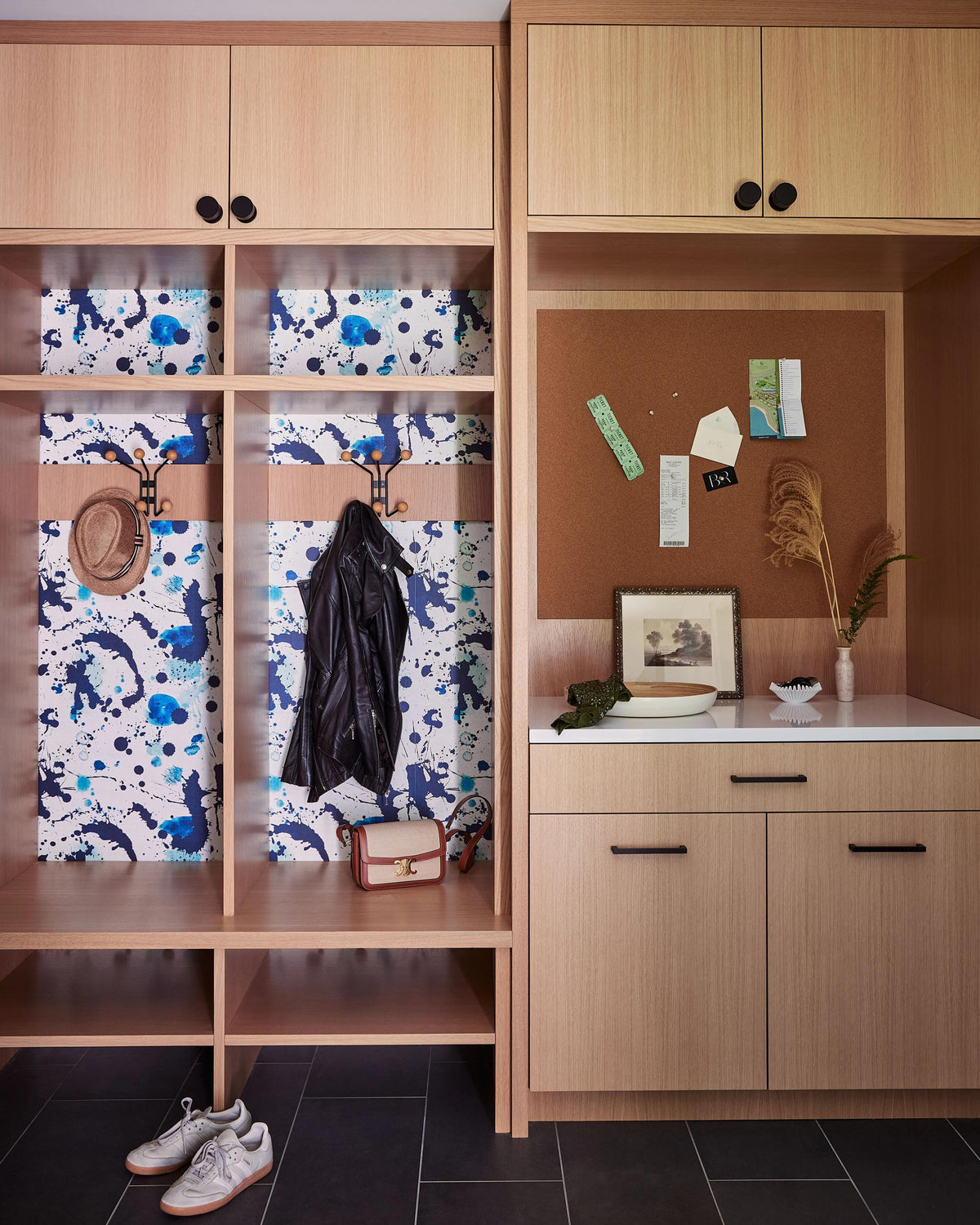 Mudroom with wood cabinetry, colorful abstract patterned shelving, corkboard, and personal belongings
