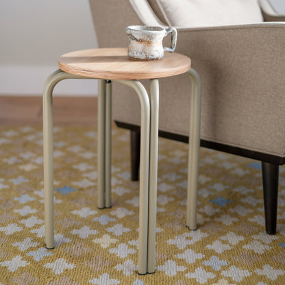 Close-up of Forma Stool showcasing white oak round top with exposed plywood edge and powder-coated steel legs beside an upholstered chair