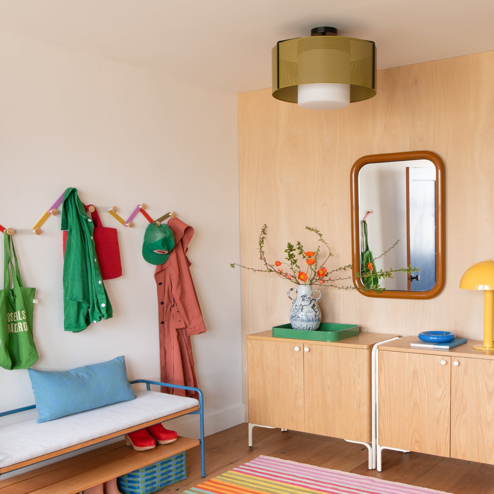 Swell 20-inch flush mount ceiling light with perforated olive metal shade and frosted glass diffuser installed in an entryway with a wood cabinet, mirror, and colorful hooks