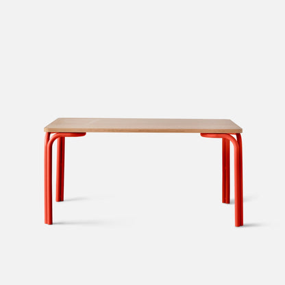 Front view of Forma Dining Table showcasing oak veneer top and red powder-coated steel legs with white background