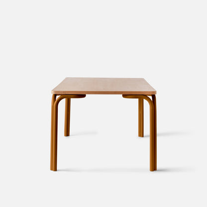 Front view of Forma Dining Table showcasing light oak veneer top and curved gold powder coated steel legs with a white background