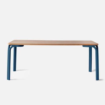 Front view of Forma Dining Table showcasing oak veneer top and blue powder-coated steel legs with a white background