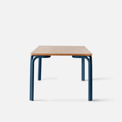 Front view of Forma Dining Table showcasing a wooden top and blue powder-coated steel legs against a white background