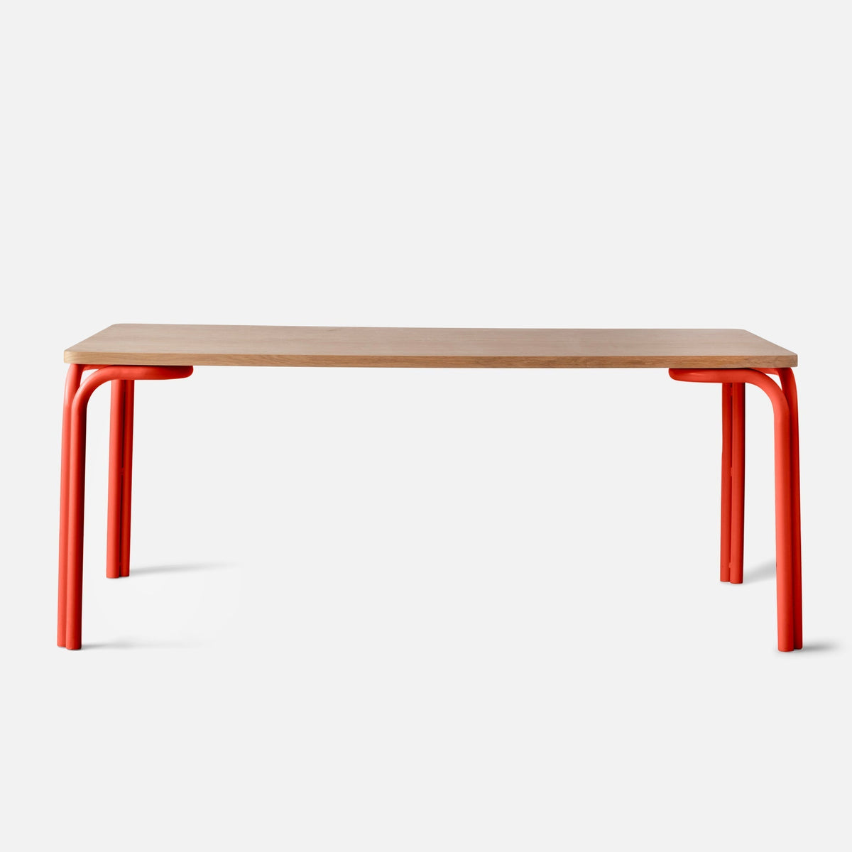 Front view of Forma Dining Table showcasing oak veneer top and red powder-coated steel legs on a white background