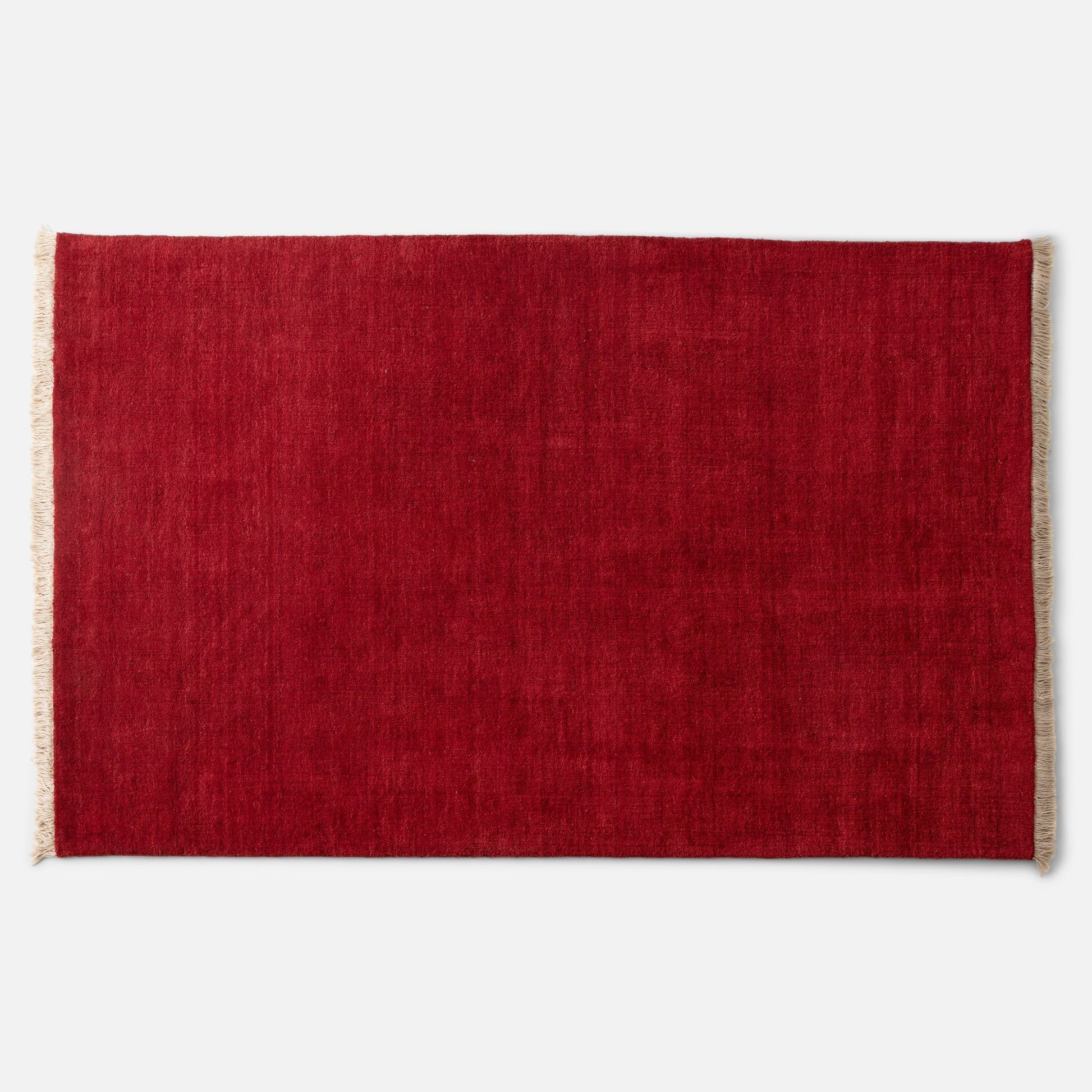 Top-down close-up of Mesa Wool Rug showing deep red hand-loomed wool pile and natural fringe against white background