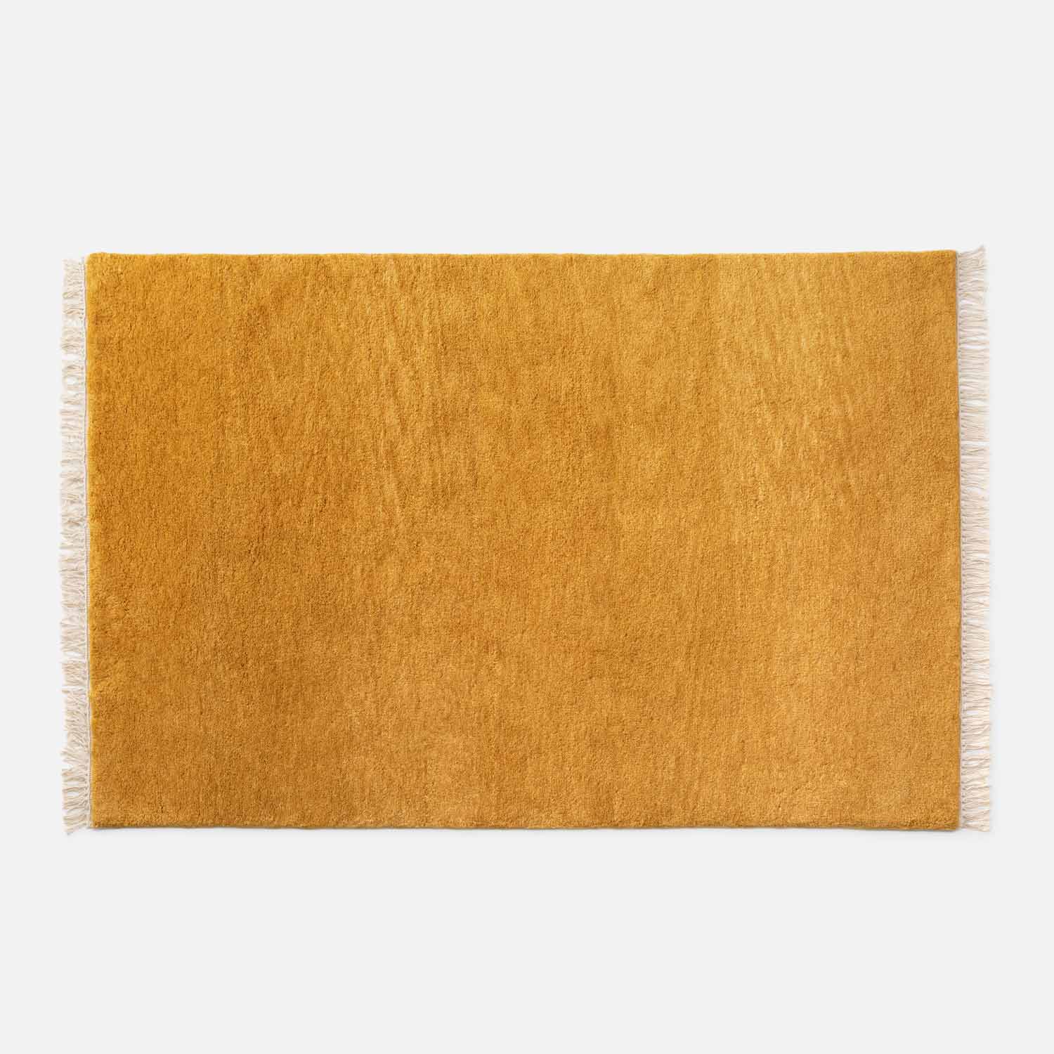 Top view of Mesa Wool Rug showcasing golden hand-loomed cut pile and ivory fringe on white background