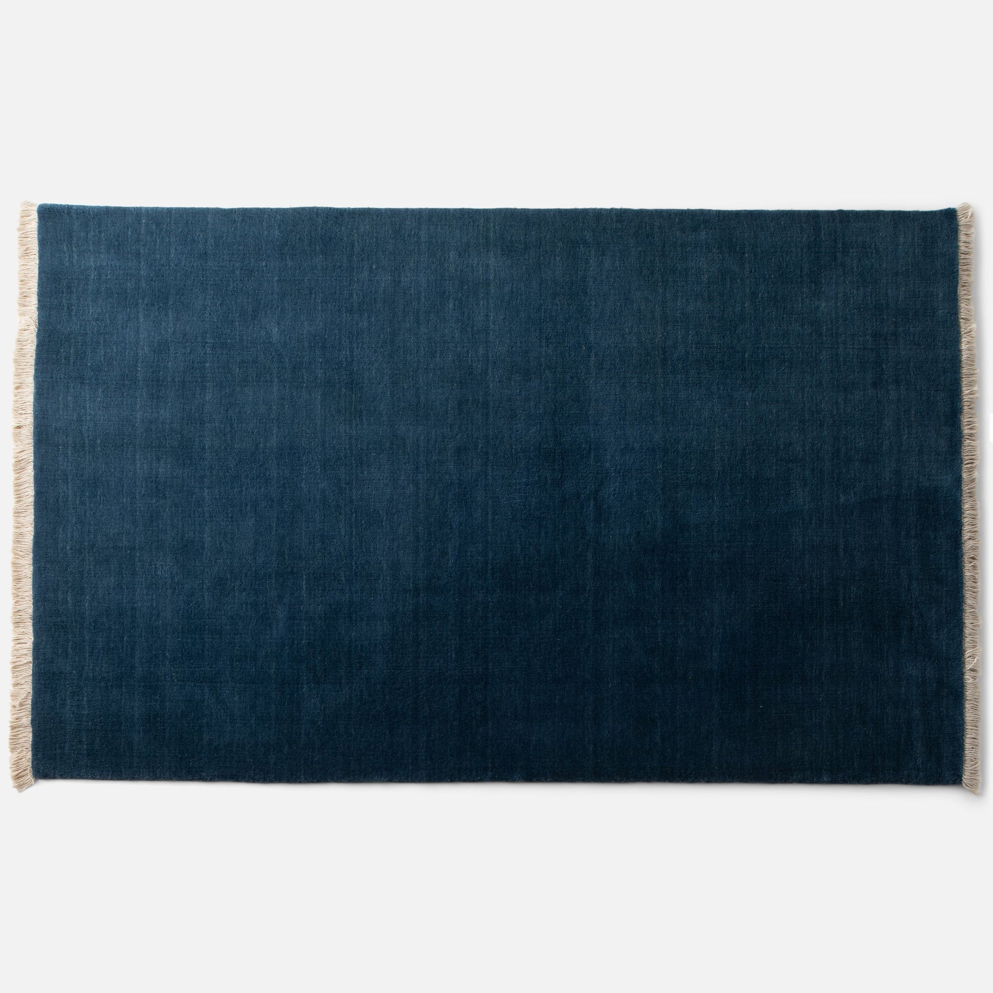 Top view of Mesa Wool Rug in green showcasing hand-loomed cut pile and natural fringe on a white background