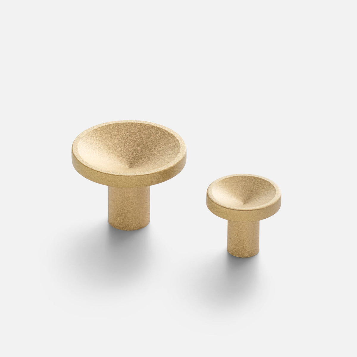 Angled view of Rhone Knob in cast brass showcasing recessed textured faces and two sizes on a light background