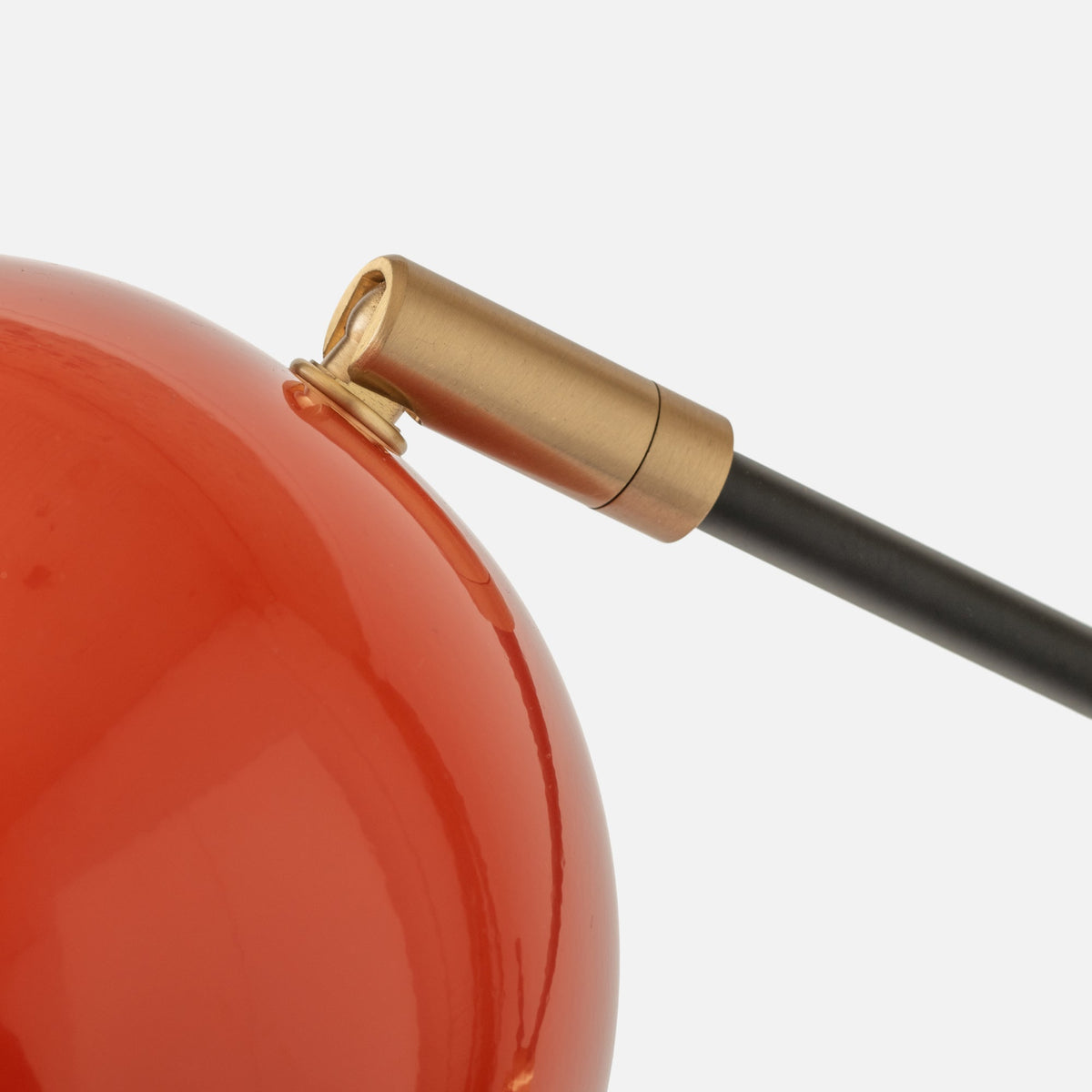 Close-up of Isaac Desk Lamp showcasing its brass swivel, black arm, and red shade on a white background