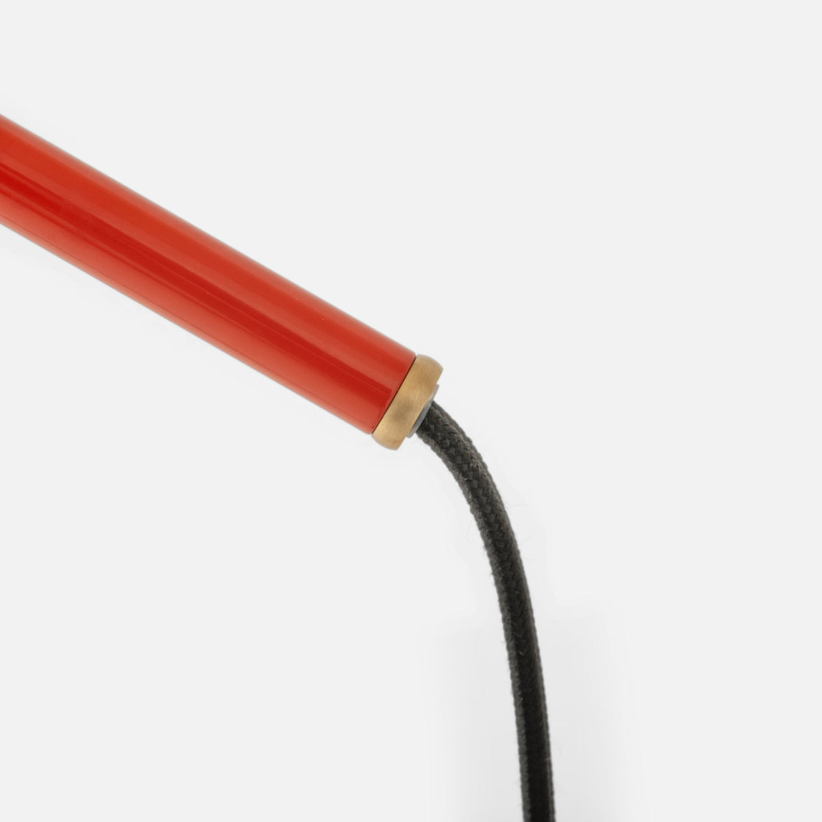 Close-up view of Isaac Desk Lamp showcasing red steel arm, brass swivel, and braided black cord on a white background
