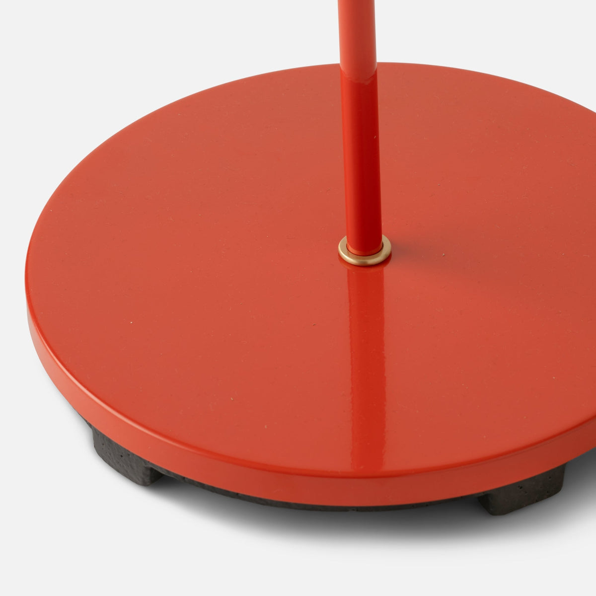 Close-up of Isaac Desk Lamp showcasing its red steel base, brass swivel, and cast-iron underside on white background