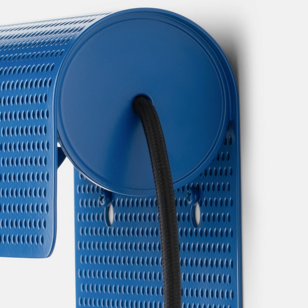 Close-up view of the Swell Plug-In Sconce in cobalt-satin showing its perforated steel shade and black cord