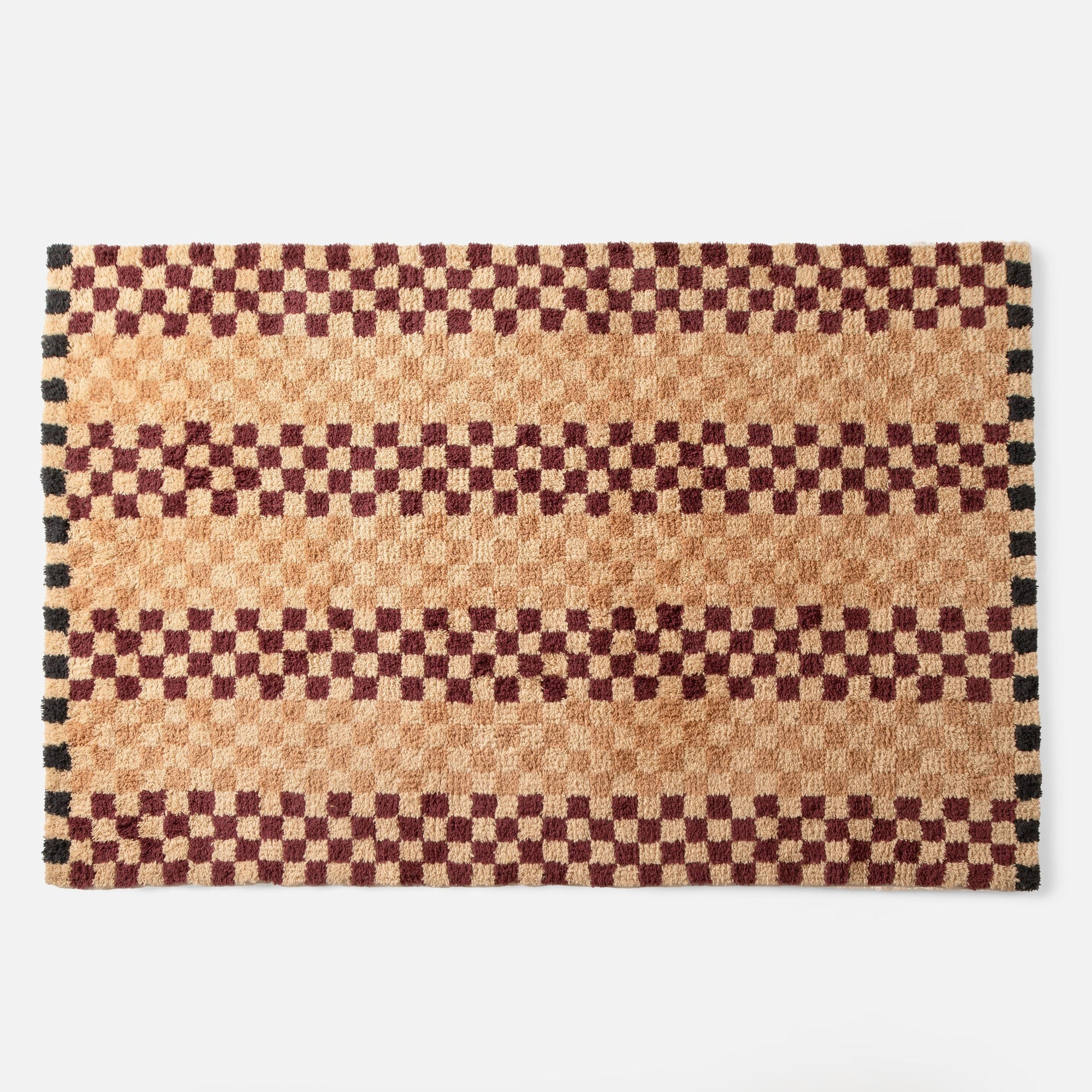 Top edge of Schoolhouse x Clare V. Felix shag wool rug showing butterscotch and burgundy checkered pattern with black border on white background