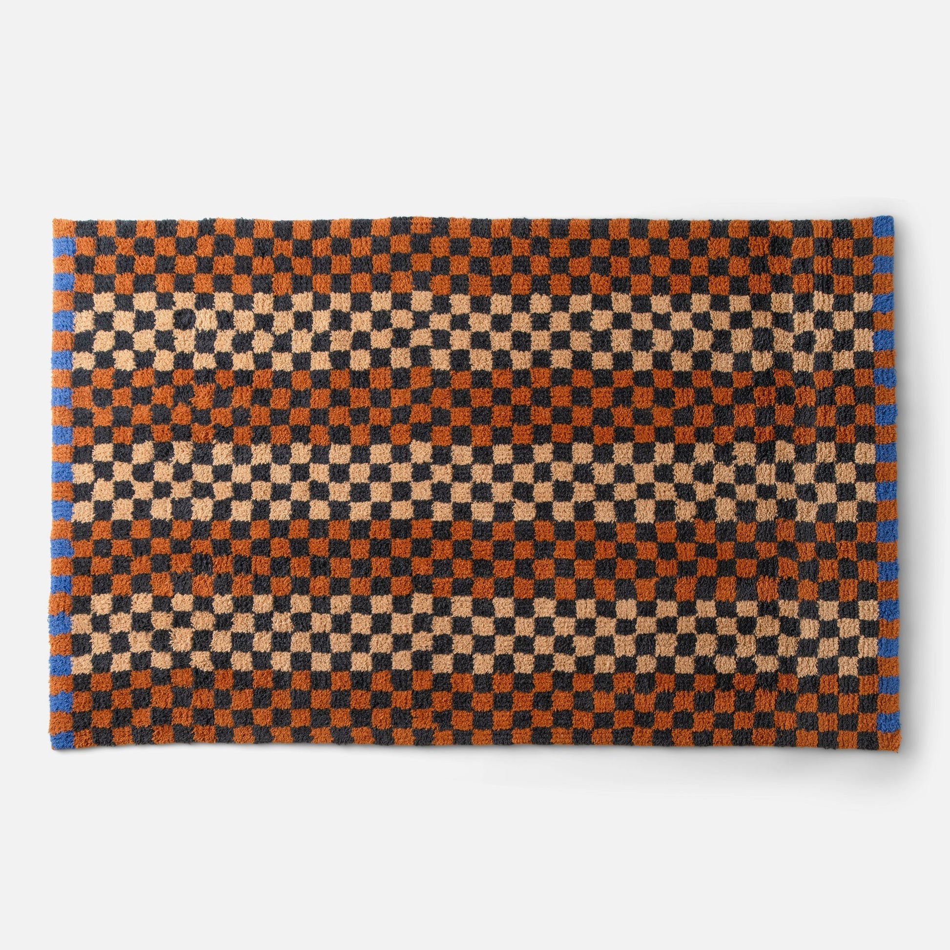 Top-down view of Schoolhouse x Clare V Felix shag wool rug showcasing checkerboard pattern in butterscotch, rust and black on white background