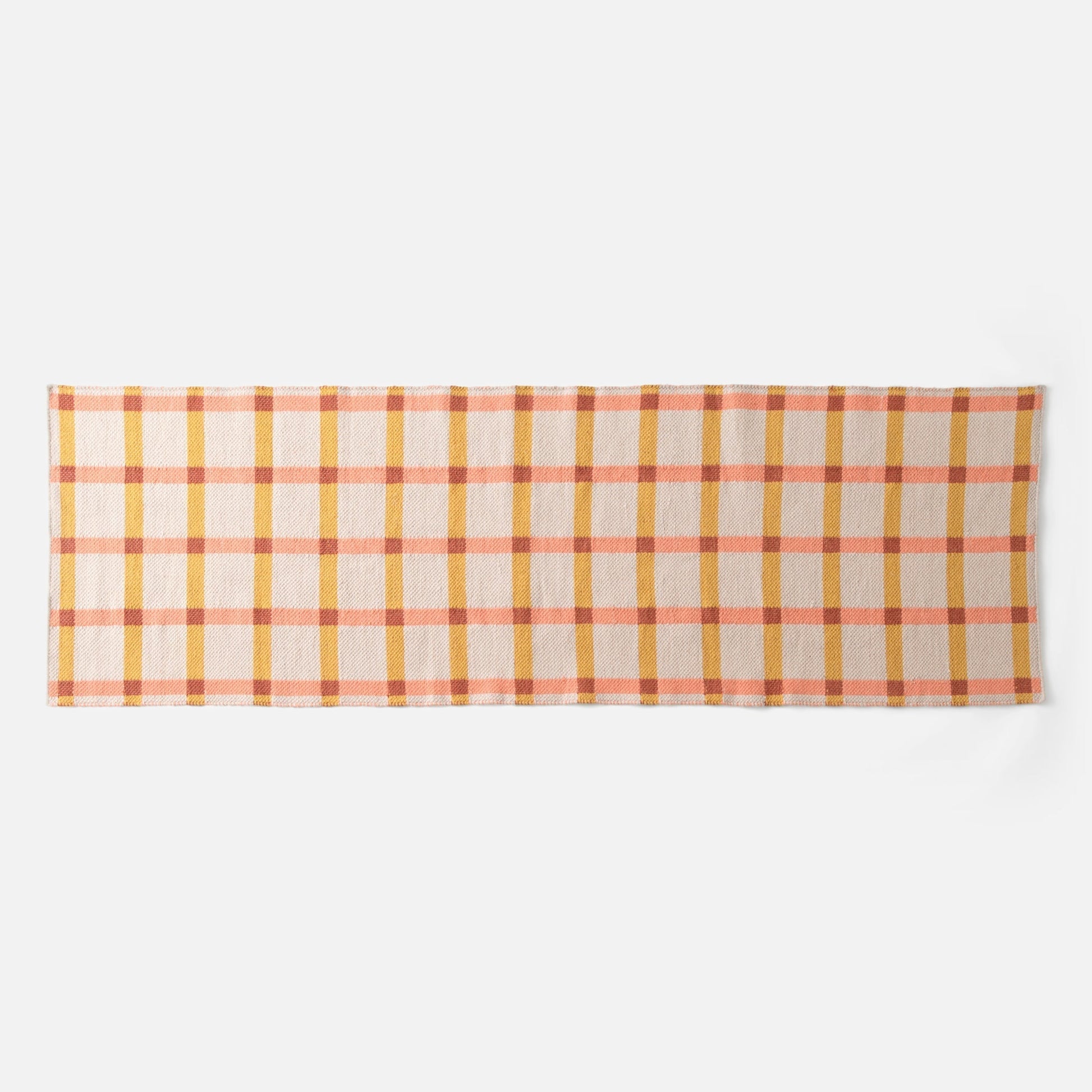 Flat lay of Plaid Wool Reversible Rug showcasing peach, mustard, and rust plaid on a white background