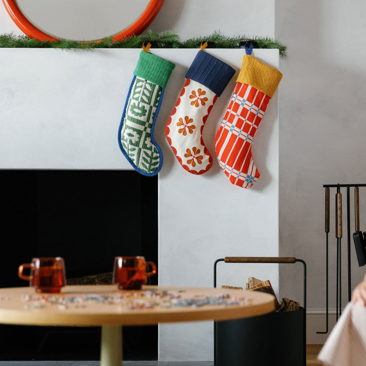 Three colorful holiday stockings hang beneath greenery in a modern living room