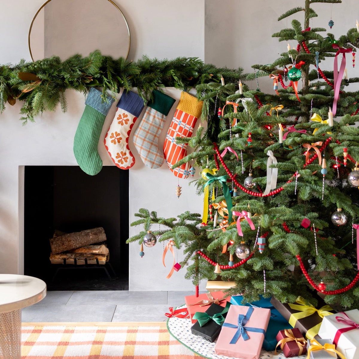 Holiday mantel displays colorful stockings beside a decorated Christmas tree
