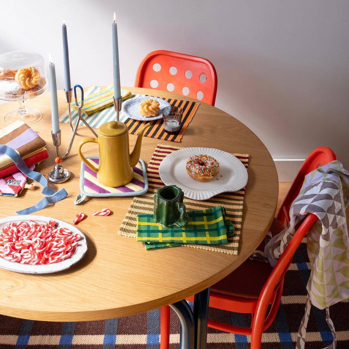 Loop Candelabra decorates a festive dining table with candles, colorful place settings, treats, and red chairs