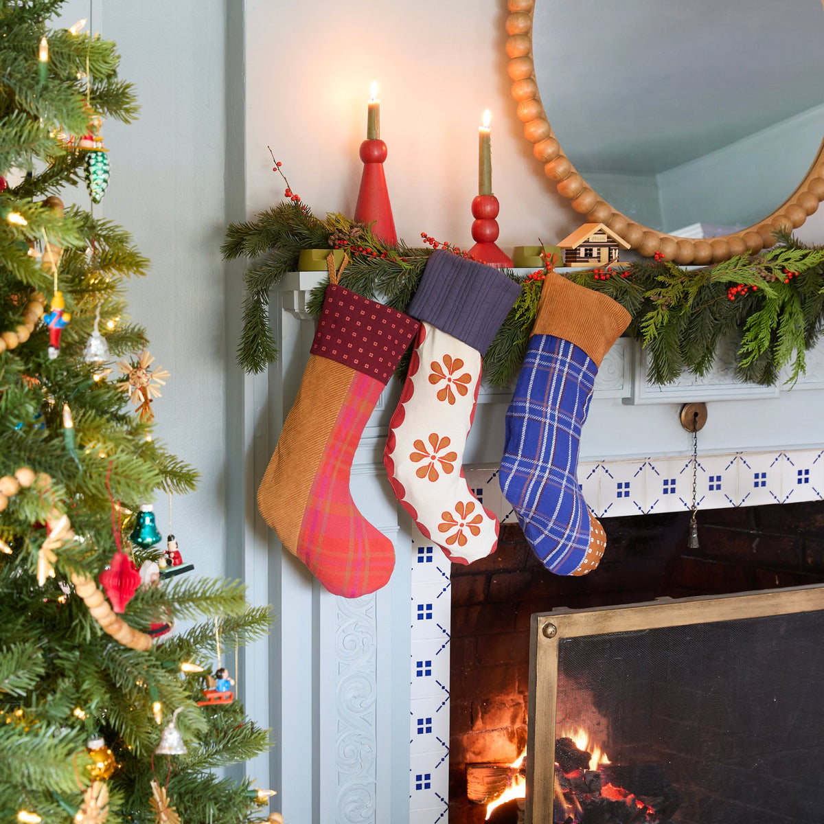 Swiss Scallop Stocking hanging from a garlanded fireplace beside a decorated Christmas tree