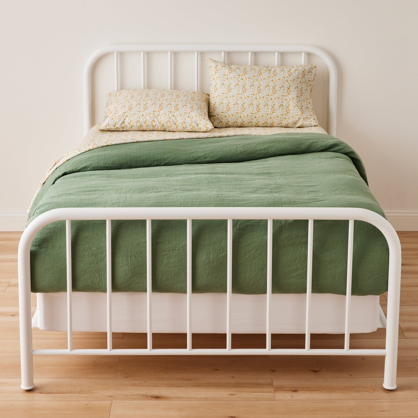 Front of Wallowa Floral percale pillowcase set showcasing chamomile print on bed with green duvet and white frame