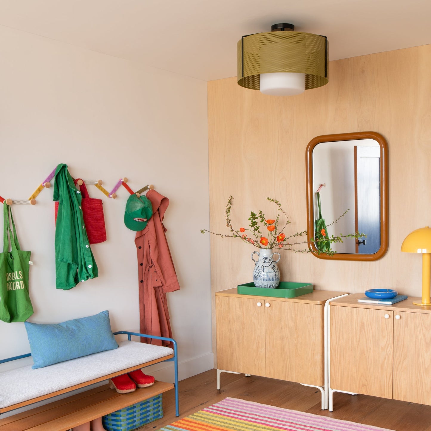 Colorful striped Lisse Performance Rug on an entryway floor beside a wood cabinet, mirror, bench, and wall hooks