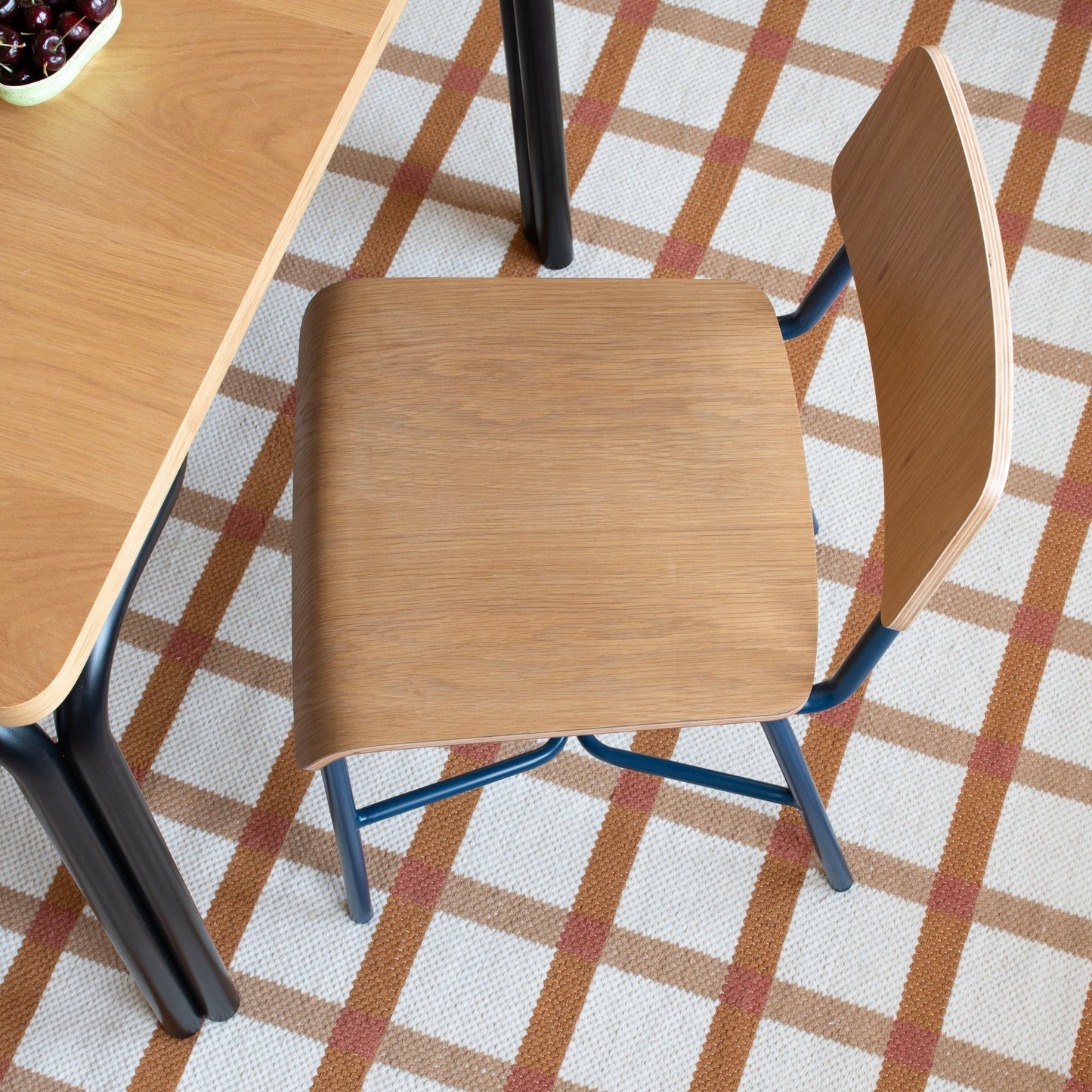 Top-down view of Plaid Wool Reversible Rug showing tan and rust plaid on white woven wool under a wooden chair and table
