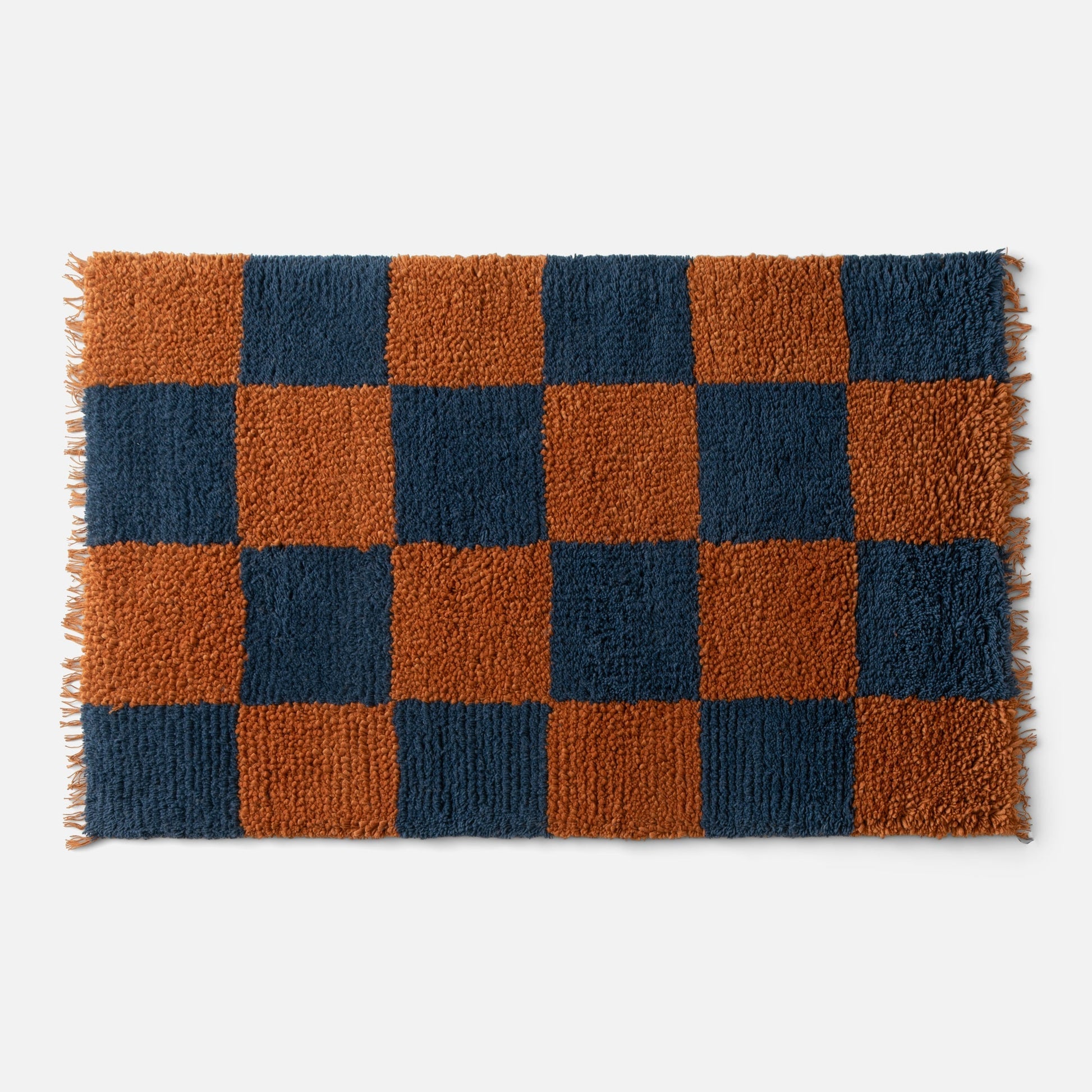 Top-down view of Jacques shag wool rug showcasing indigo and rust checkerboard shag pile with fringe on light gray background