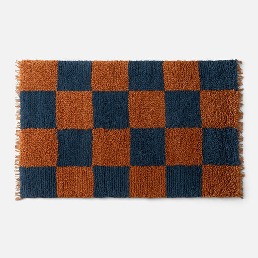 Top-down view of Jacques shag wool rug showcasing indigo and rust checkerboard shag pile with fringe on light gray background