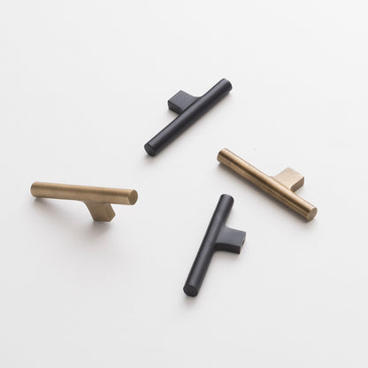 Flat lay of Galley Pulls in natural brass and matte black showing cylindrical T bar shape and square backplate on white background