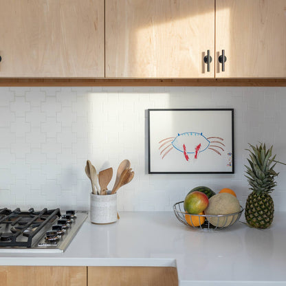 Two matte black Galley Pulls mounted on light maple cabinet doors above a white tiled backsplash in a bright kitchen