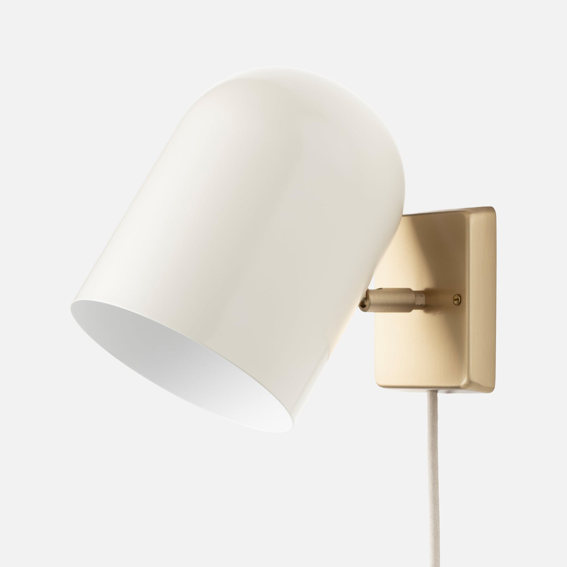 Angled close-up of Allegheny 6 inch plug-in sconce showcasing white metal shade, brass rectangular wall plate, and fabric cord on white background